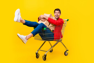 Full length body size view of attractive cheery guy sitting inside cart carrying buyings isolated...