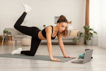 Fototapeta premium Sporty African Female Exercising Near Laptop On All Fours Indoors