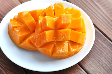 Ripe mango with juicy pulp cut into pieces on a white plate on a wooden table