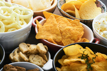 Unhealthy food or snacks. All classic potato snacks with peanuts, popcorn and onion rings and salted pretzels in bowl plates on old wooden background. Unhealthy food for figure, heart, skin, teeth.