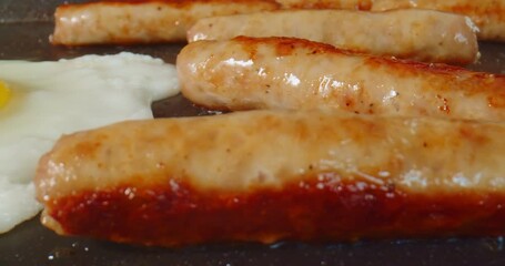 Macro probe footage of breakfast sausage and eggs being cooked on a griddle. 4K slider shot.