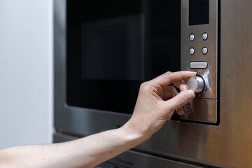 Person's hand adjusting microwave oven mode in kitchen