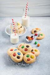 Homemade cookies with colorful chocolate candies and milk. Stack of shortbread cookies with multi colored candy on plate with bottle of milk on light gray background. Baby food concept. Copy space.
