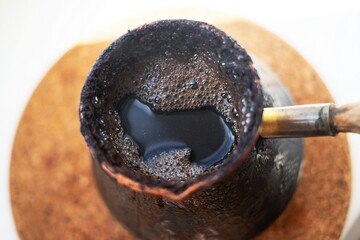 invigorating coffee in an old turk on the window and a wooden stand on a bright spring morning draws a heart on the surface