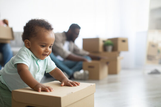 Happy black family relocating to new apartment, boy pushing box