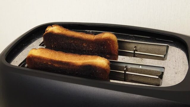 Slow motion. The bread burned in the kitchen toaster. Dangerous junk food concept. Bread pops out of the toaster.
