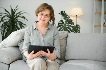 Obraz premium Smiling senior woman at home connected on internet
