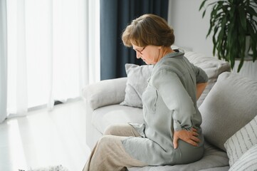 Obraz premium old age, health problem and people concept - senior woman suffering from pain in back or reins at home
