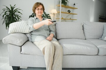 people, television and entertainment concept - senior woman in eyeglasses with remote control watching tv at home