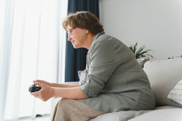 Older person having fun playing a console with a video game sitting on the sofa.