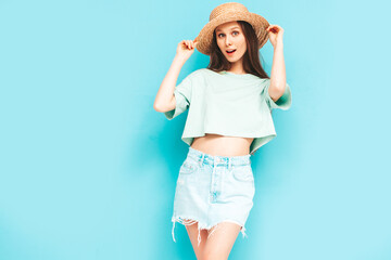 Obraz na płótnie Canvas Portrait of young beautiful smiling female in trendy summer jeans skirt. carefree woman posing near blue wall in studio. Positive model having fun indoors. Cheerful and happy. In hat