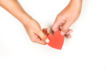Mano de mujer y de hombre sosteniendo un corazón de papel rojo sobre un fondo blanco liso y...