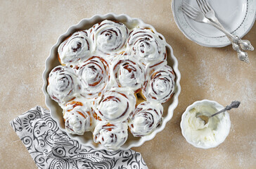 Cinnamon rolls or cinnabon, homemade sweet traditional dessert buns with white cream sauce on biege background, copy space. top view