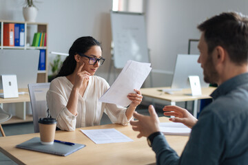 Personnel manager communicating with vacancy candidate, reading resume during job interview at office