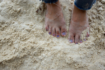 The feet and legs of tourists wearing jeans. standing on a beautiful sandy beach
