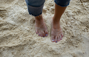The feet and legs of tourists wearing jeans. standing on a beautiful sandy beach
