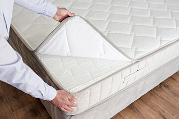 Cropped shot of man showcasing the waterproof topper for white orthopedic mattress. Male showing hypoallergenic foam matress protector. Close up, copy space, top view, background. - obrazy, fototapety, plakaty