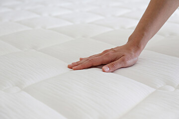 Cropped shot of young woman's hand testing white orthopedic matress on firmness. Female pressing...