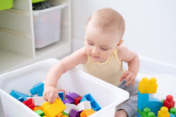 Cute kid girl playing in colorful plastic constructor on floor at home. Early childhood development