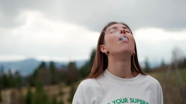 girl smokes an electronic cigarette on a background of mountains