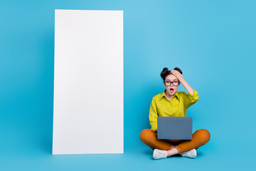 Full length portrait of impressed confused lady sit floor hand forehead huge phone isolated on blue color background