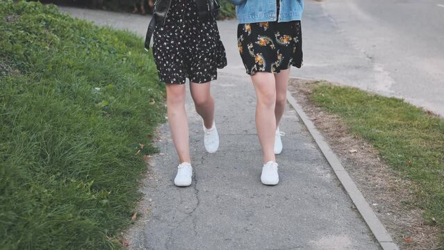 Two girlfriends in white sneakers walk down the street.