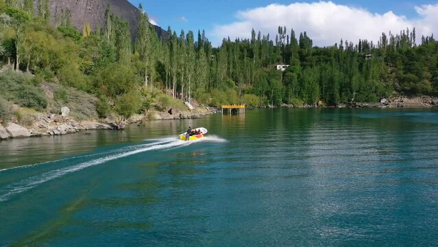 aerial drone of pakistani tourists in the mountain forest of Skardu Pakistan taking a motor boat ride on beautiful blue water at Upper Kachura Lake on a sunny summer day