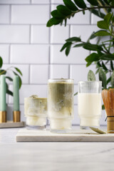 tall rippled glass with matcha latte - japanese green tea powder and whipped milk on marble board in white kitchen