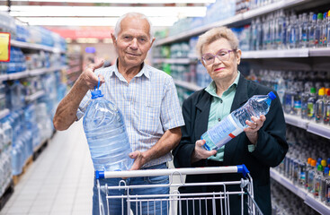 mature european spouses selects bottled water in the department of supermarket