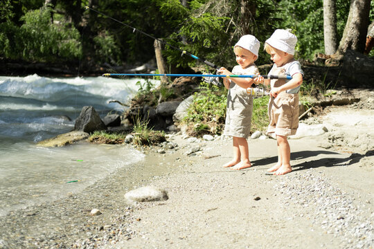 two kids boys brothers twins fishing with a fishing rod on the mountain river on summer day