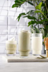 tall rippled glass with matcha latte - japanese green tea powder and whipped milk on marble board in white kitchen