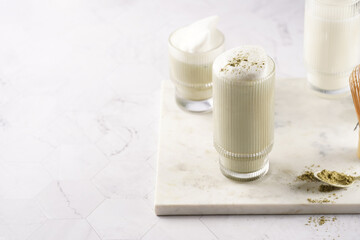 tall rippled glass with matcha latte - japanese green tea powder and whipped milk on marble board in white kitchen
