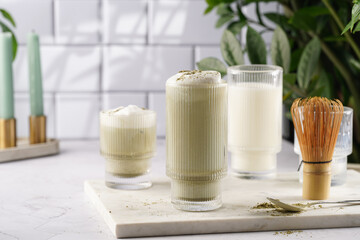 tall rippled glass with matcha latte - japanese green tea powder and whipped milk on marble board in white kitchen