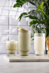 tall rippled glass with matcha latte with splashes - japanese green tea powder and whipped milk on marble board in white kitchen
