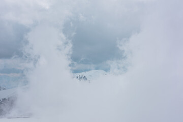 Fototapeta na wymiar Awesome aerial view to high snowy mountain in dense low clouds. Minimal landscape with beautiful mountain peak in thick clouds. Simple minimalism with snow mountain top in cloudy sky above low clouds.
