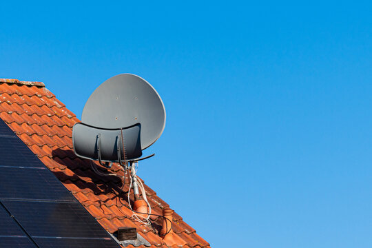 Satellite dish on the roof of a house covered with terracotta tiles. Solar panels on the roof. Blue sky.
