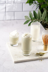tall rippled glass with matcha latte - japanese green tea powder and whipped milk on marble board in white kitchen