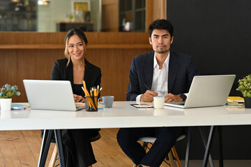 A portrait of happy Asian businesspeople working together on laptops in the office, for business and technology concept.