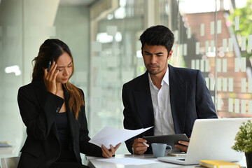 Portrait of serious Asian businesspeople working together on a document, a tablet and a laptop in the office, for business and technology concept.