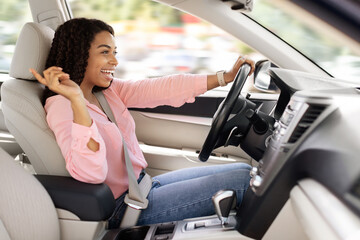 Happy black woman enjoying music driving luxury car