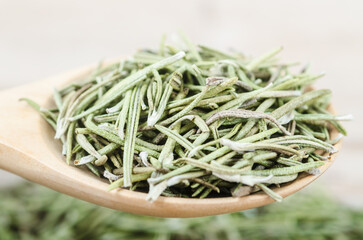 Dried rosemary spice in wooden spoon. Macro with shallow depth of field.