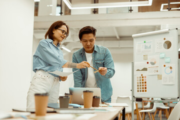 Two colleagues standing in the office and holding documents