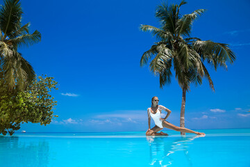 Elegant woman in white swimsuit in pool on tropical Maldives island. Beautiful bikini body girl in pool with view on horizon. Elegant model near the pool on beautiful Indian ocean landscape. Travel