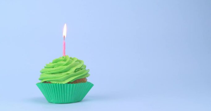 Tasty birthday cupcake with burning candle on light blue background