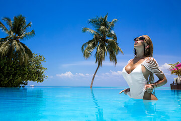 Elegant woman in white swimsuit in pool on tropical Maldives island. Beautiful bikini body girl in...
