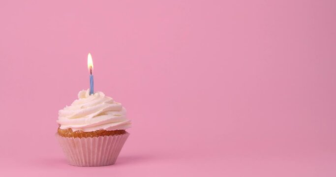 Tasty birthday cupcake with burning candle on pink background