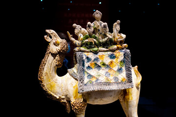 Closeup of musicians sitting on a camel figurine on a dark background