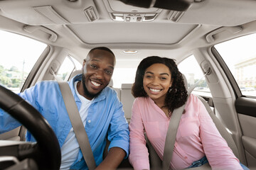 Happy black couple sitting in car posing at camera