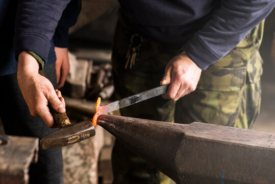Blacksmith forges hinge on a anvil. Hammering hot red steel