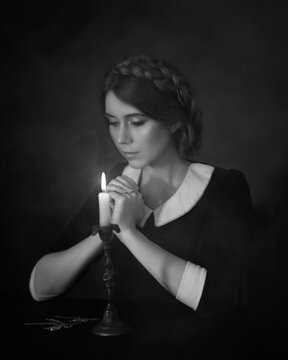 Praying girl in a black dress over a burning candle in black and white format